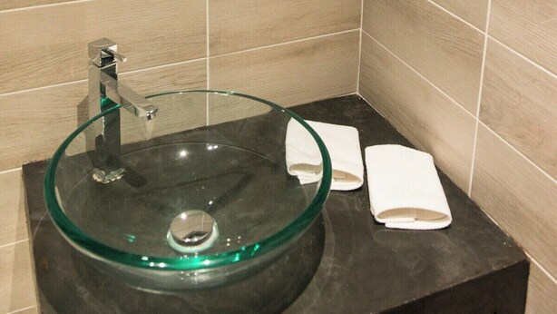 A bathroom with a hexagonal mirror, a glass sink, and a towel rack.