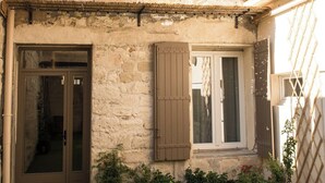 A stone building with a front door, two windows with shutters, and a small balcony.