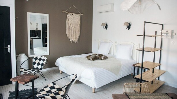 Ein Schlafzimmer mit einem Bett, einem Sessel, einer Wanddekoration aus Makramee, einer Stehlampe und einem Holzregal.
