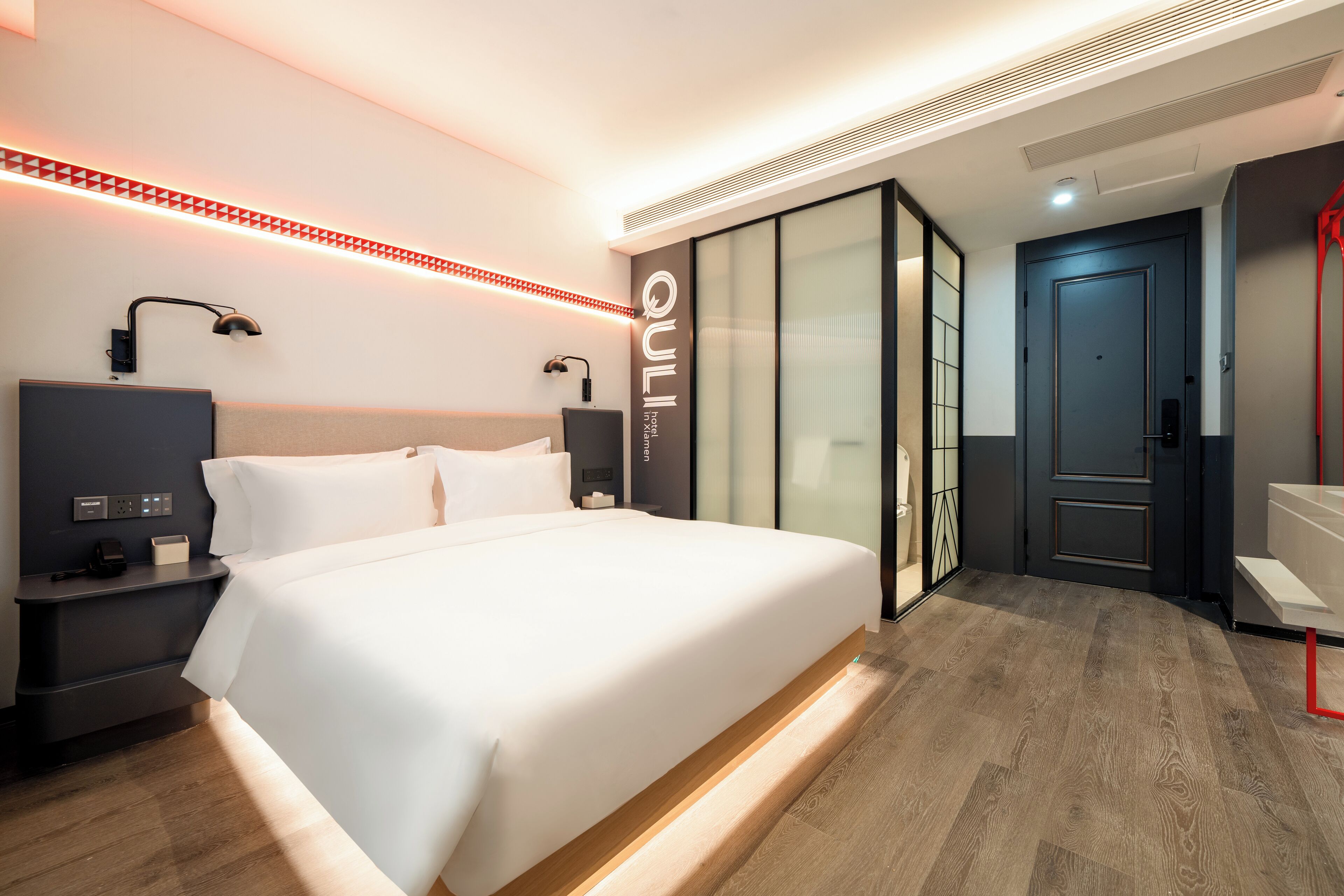 A modern hotel room with a large bed, bedside tables, a desk, and a wardrobe with sliding doors.