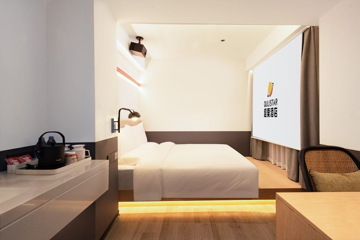 A hotel room with a bed, bedside table, lamp, and a large window with curtains.
