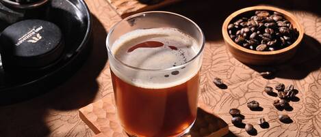 A glass of amber beer on a wooden coaster, surrounded by coffee beans and a coffee grinder.