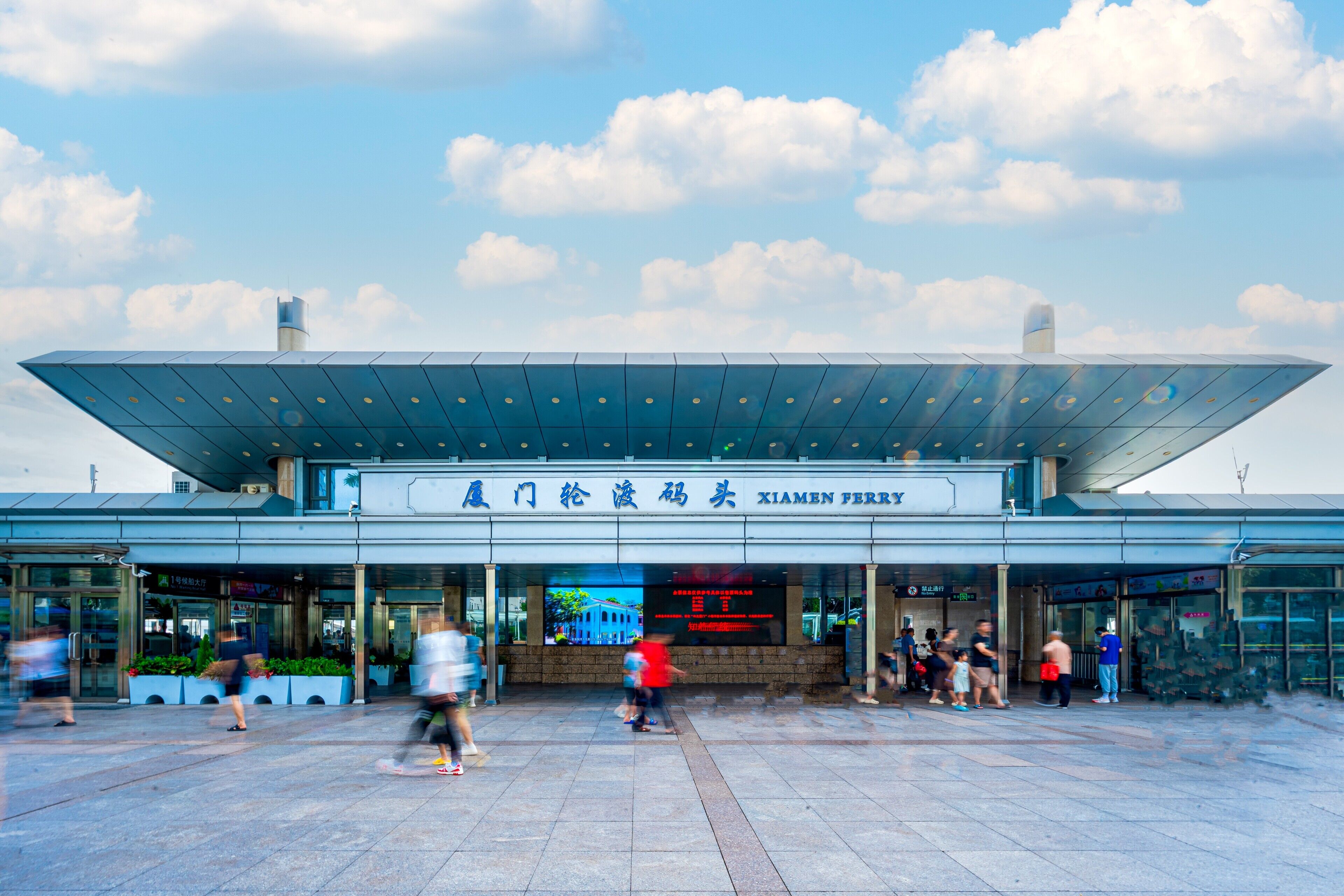 A modern building with a large glass entrance and a sign reading "Xiamen Ferry".