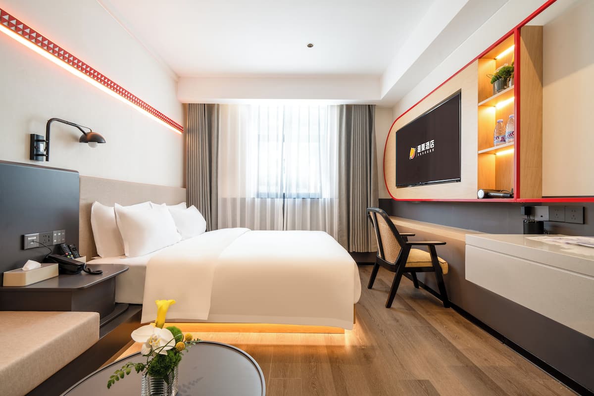 A hotel room with a bed, a desk, a TV, and a minibar.