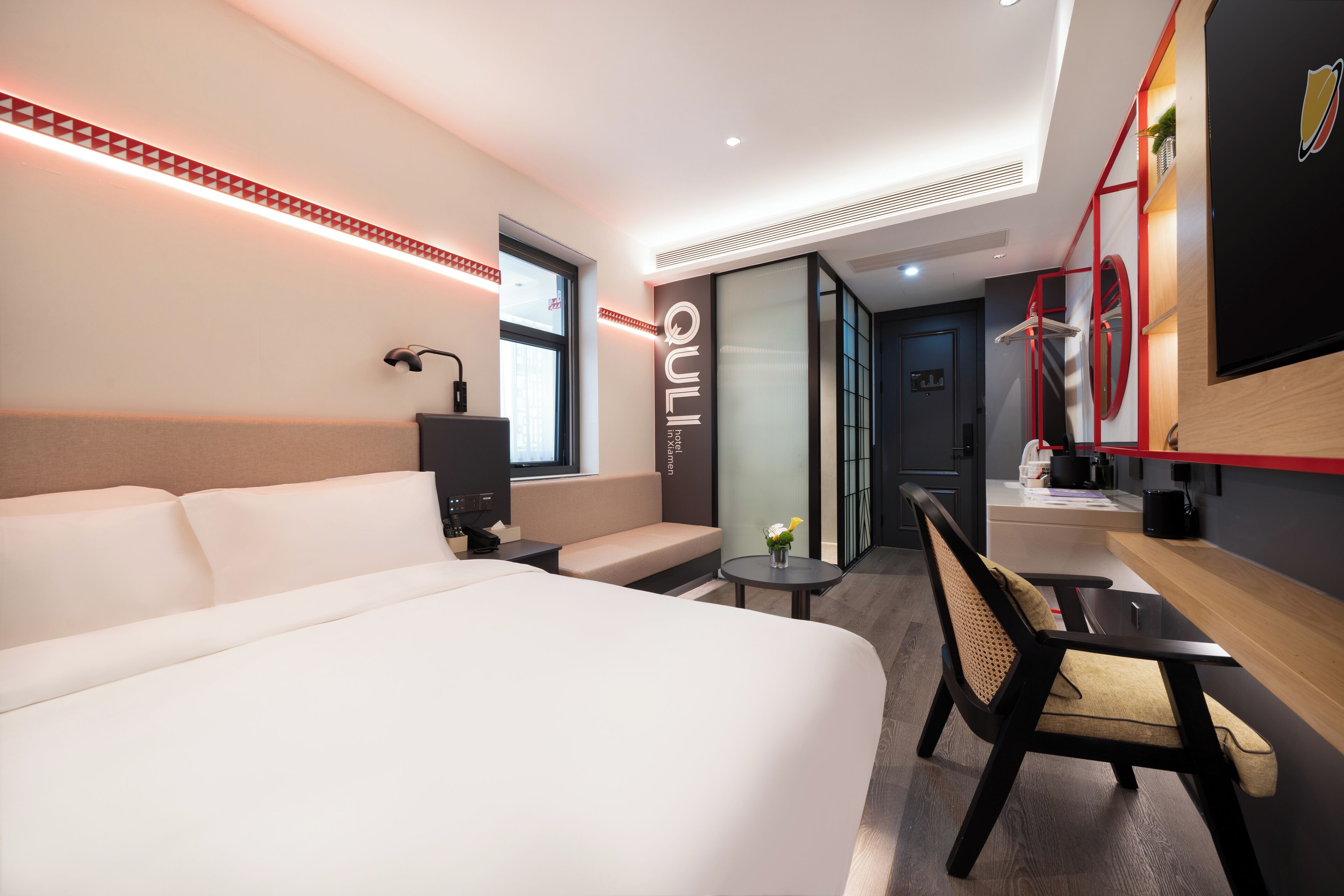 A modern hotel room with a large bed, a seating area, a desk, and a TV mounted on the wall.