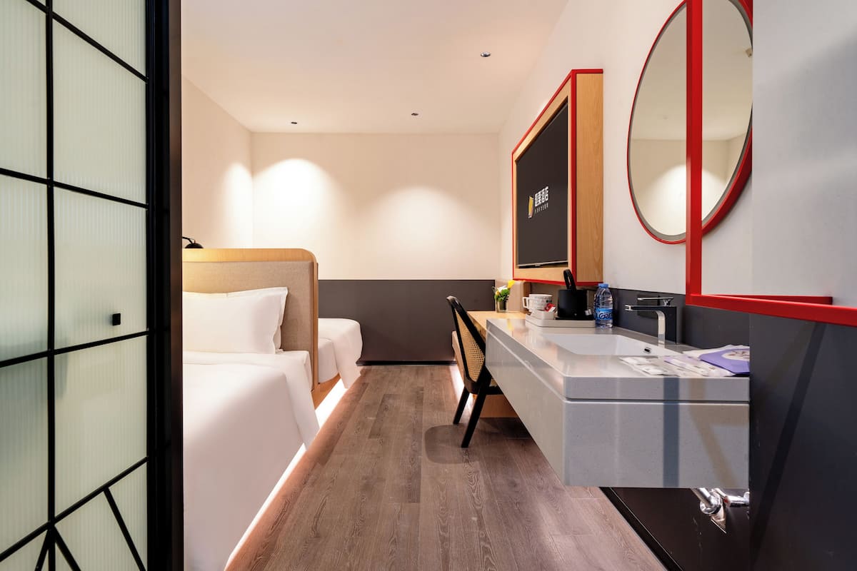 A hotel room with a bed, a desk, a chair, a mirror, a sink, and a wardrobe.