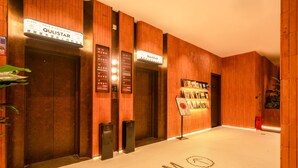 A hotel lobby with wooden paneling, two elevators, and a sign indicating the room rate. - XIAMEN ZHONGSHAN ROAD  QULISTAR HOTEL (Xiamen)