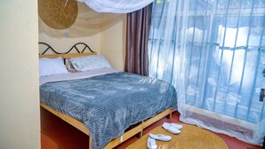 Ein Bett mit blauer Decke, Moskitonetz und einer gewebten Matte auf dem Boden.