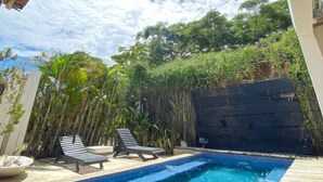 A swimming pool with wooden decking, lounge chairs, and a bamboo backdrop. - Hotel Casa Kai (Dibulla)