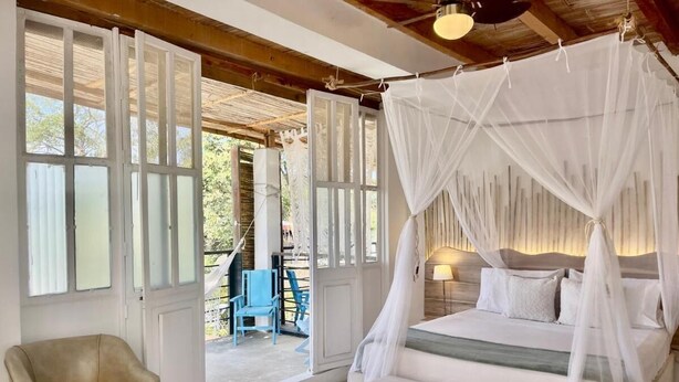 A bedroom with a four-poster bed, a chair, and a view of the outside. - Hotel Casa Kai (Dibulla)