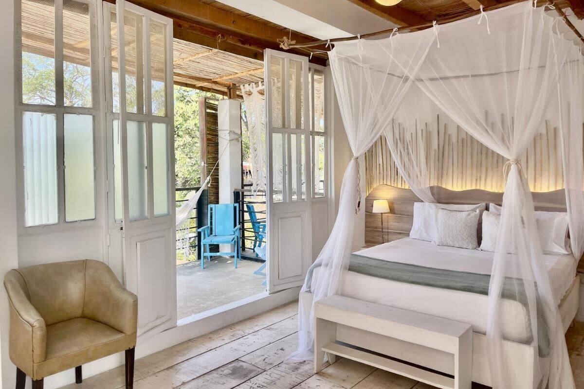 A bedroom with a four-poster bed, a chair, and a view of the outside.