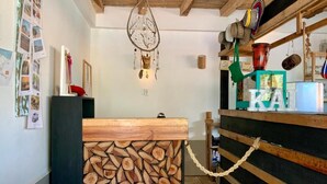 A rustic interior with a wooden log wall, a hanging dreamcatcher, and a shelf with decorative items. - Hotel Casa Kai (Dibulla)