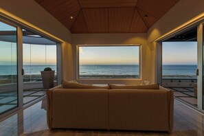 Un saló modern amb una finestra gran que dona a l'oceà, un sostre de fusta i un sofà beix.