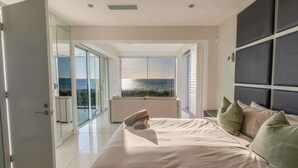 Een slaapkamer met een bed, kussens, uitzicht op zee en een balkon.
