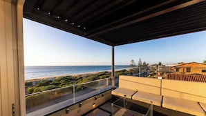 A balcony with a glass railing overlooking a beach and ocean.