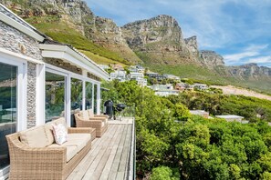 Un balcón con mobiliario de mimbre, con vistas a un paisaje montañoso y una zona residencial.