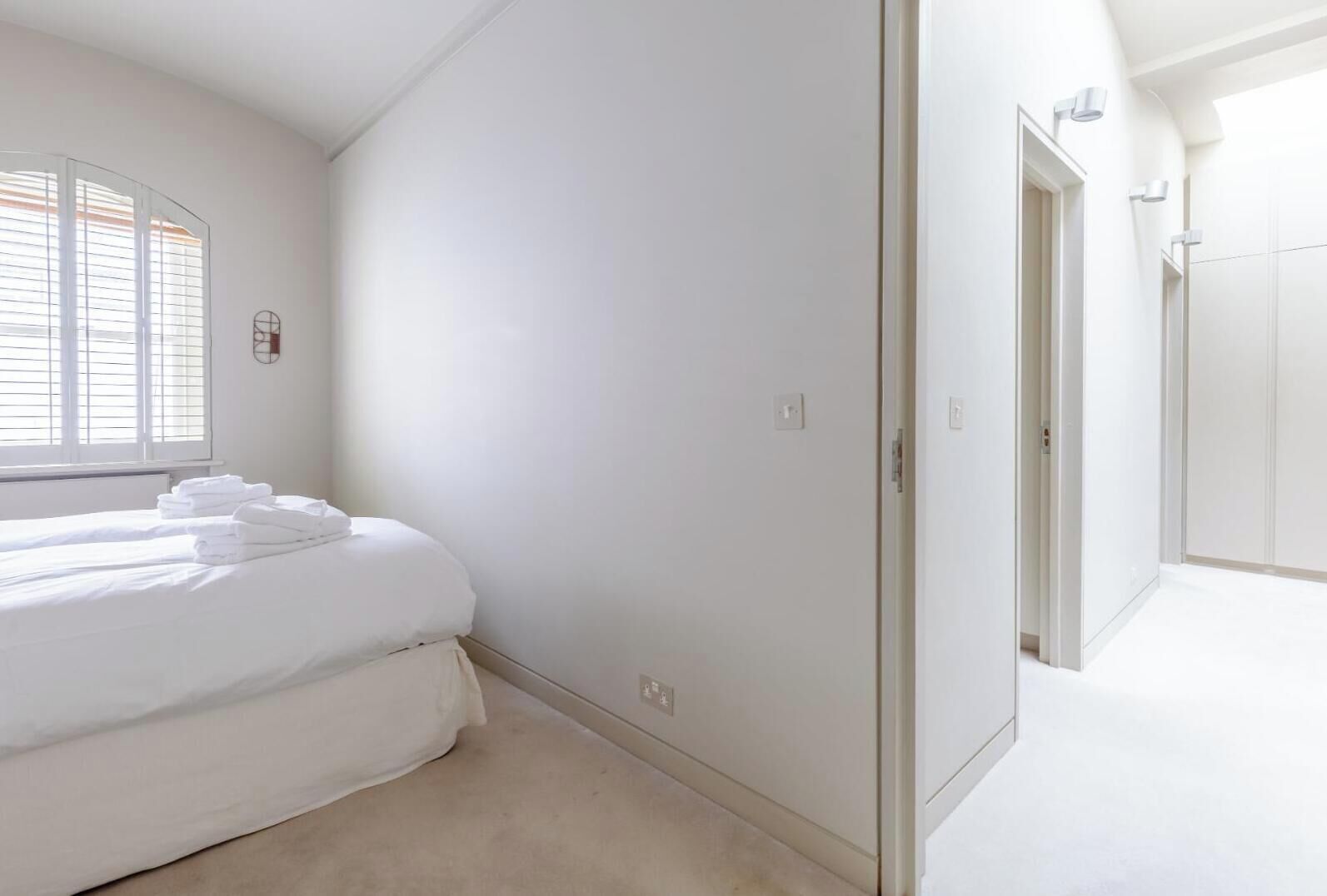 A bedroom with a bed, a window with blinds, a door, and a hallway.