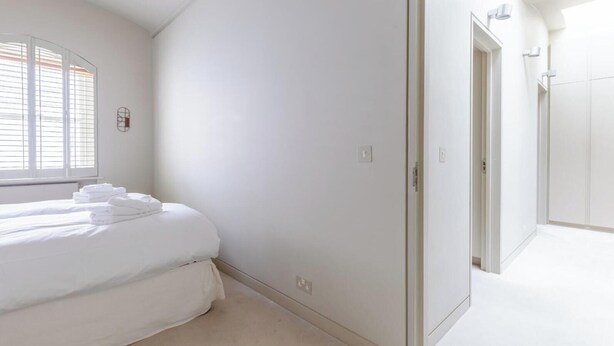 Una camera da letto con un letto, una finestra con persiane, una porta e un corridoio.