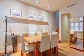 A modern dining area with a wooden table and white chairs, a metal sculpture, and framed pictures on the wall.