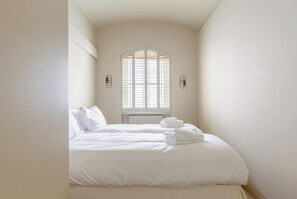 A bedroom with a bed, a window with blinds, and a small table.
