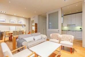 Un salon moderne comprenant un canapé, des fauteuils, une table à manger et un coin cuisine avec des placards et une fenêtre.