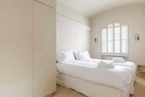 Une chambre avec deux lits, une grande fenêtre avec des stores et une armoire.
