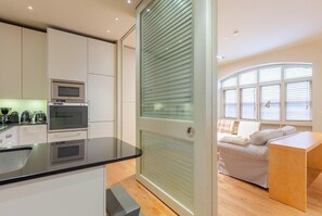 A modern kitchen with built-in appliances, a dining area with a wooden table, and a bedroom with a window view.