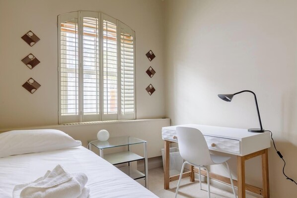 A bedroom with a bed, a desk, a chair, a lamp, and a window with blinds.
