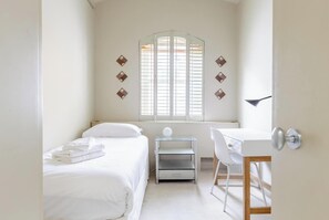 Een slaapkamer met een bed, bureau en een raam met jaloezieën.