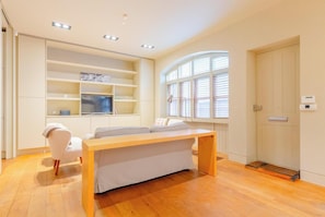 Una habitación moderna con piso de madera, un sofá blanco, una mesita, estanterías empotradas, una ventana con persianas y una puerta con manija.