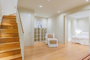 Een ruime kamer met een houten trap, een massagestoel, een bed en een witte garderobe.