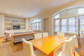 Una sala de estar moderna con una mesa de comedor de madera, sillas blancas, un sofá y estanterías empotradas.