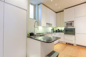 A modern kitchen with white cabinets, a black countertop, a built-in oven, and a window.