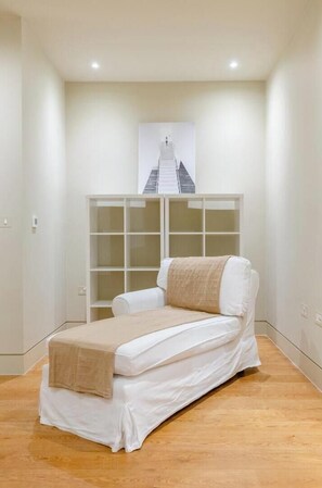 A single bed with a white mattress and beige blanket, a white wardrobe, and a framed picture of a staircase on the wall.