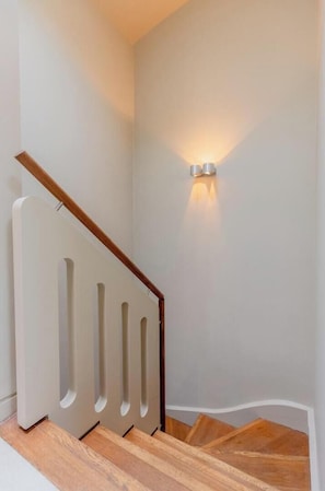 Una escalera con barandilla de madera y una pared blanca con aplique.