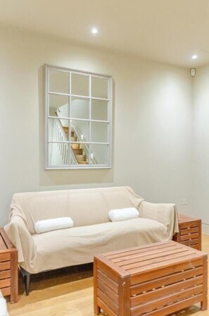 A room with a sofa, a wooden side table, a large mirror, and a staircase. - Sublime 4BD House behind V&A, South Kensington (Greater London)