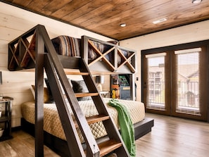 A loft-style bedroom with a bed, a ladder, and a view through a glass door.