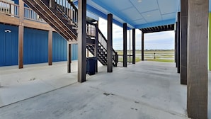 A covered outdoor area with a concrete floor, wooden columns, and a blue railing. - Heron House by Miss Kitty’s (Rockport)