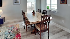A dining area with a wooden table and chairs, a rug, and artwork on the walls. - Heron House by Miss Kitty’s (Rockport)