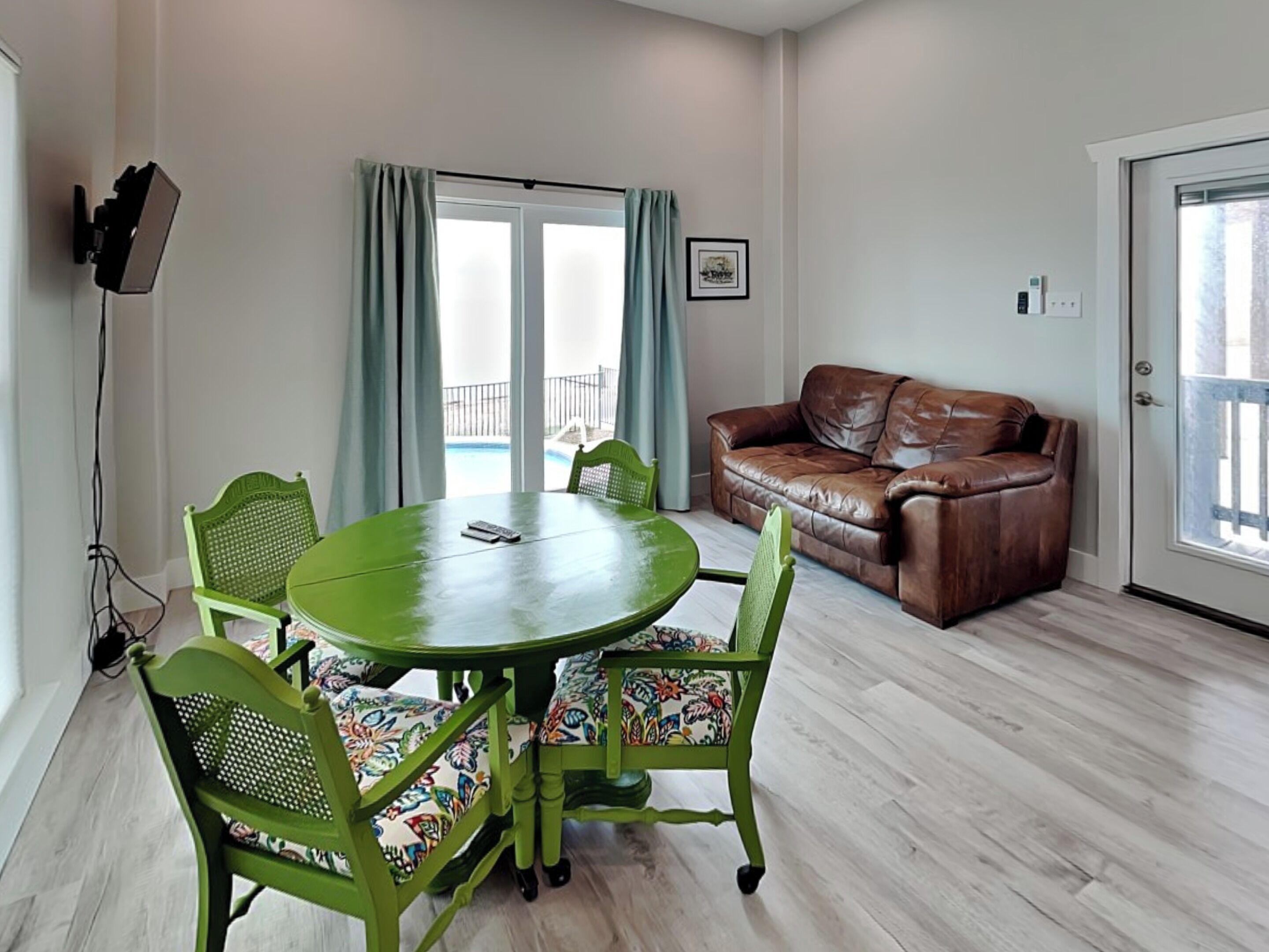 A room with a round table, two chairs, a brown leather sofa, and a large window with curtains.