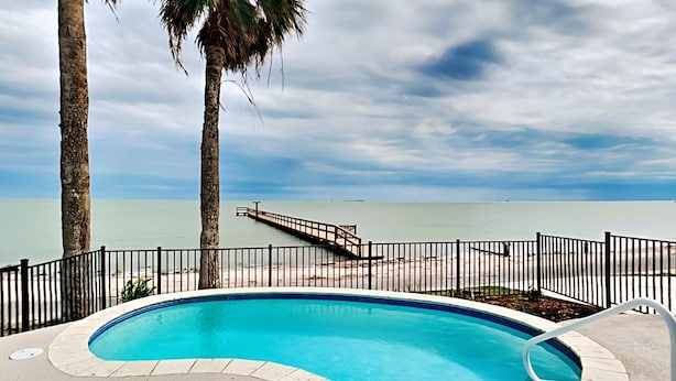 A swimming pool with a view of the ocean, surrounded by a fence and palm trees. - Heron House by Miss Kitty’s (Rockport)