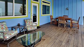 Un espacio al aire libre techado con una terraza de madera, una mesa con cubierta de vidrio y un juego de comedor.