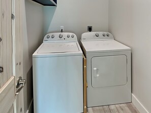 A laundry room with two stacked washers and dryers, a wooden door, and a light switch on the wall.