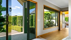Un interno moderno con ampie porte scorrevoli in vetro che si aprono su un giardino, pavimento in legno e vista su una sala da pranzo.