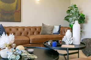 A living room with a brown leather sofa, a round coffee table, and decorative items including vases and a plant. - Watene Lodge - Spacious 5 Star Home with Pool (Taupo)