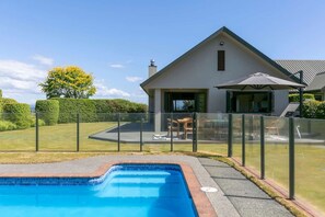 A modern house with a swimming pool, a fenced patio area, and a well-maintained lawn. - Watene Lodge - Spacious 5 Star Home with Pool (Taupo)