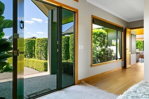 A modern interior with large sliding glass doors leading to a garden, a wooden floor, and a view of a dining area.