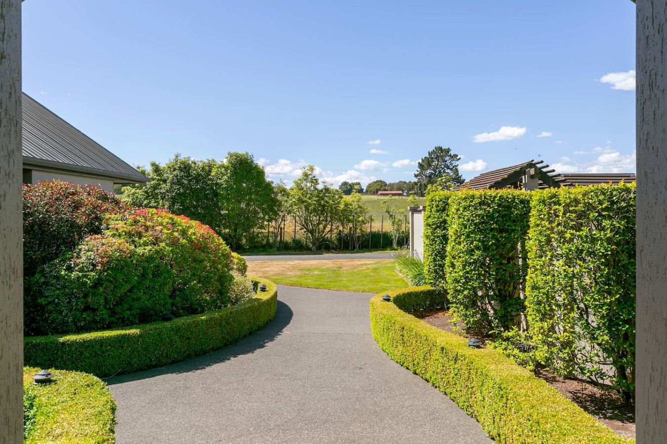 A pathway leading to a residential area with neatly trimmed hedges and a clear sky.