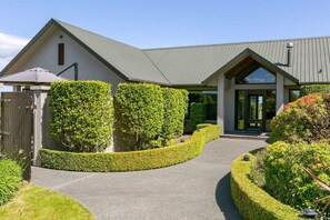 A modern house with a well-maintained garden, a paved driveway, and a metal roof. - Watene Lodge - Spacious 5 Star Home with Pool (Taupo)