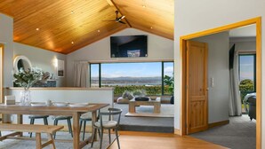 Un interno moderno con soffitto in legno, zona pranzo con tavolo e sedie, un divano e vista sull'esterno.